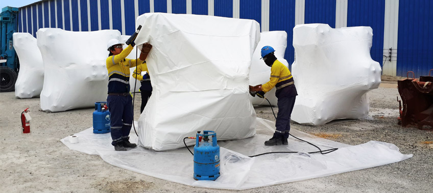 Three CEA Project Logistics Staff apply shrink wrapping to cargo